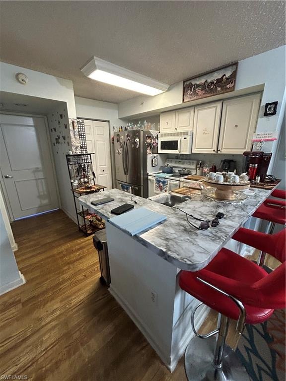 Kitchen with range, a kitchen bar, dark wood-type flooring, white fridge, and stainless steel microwave
