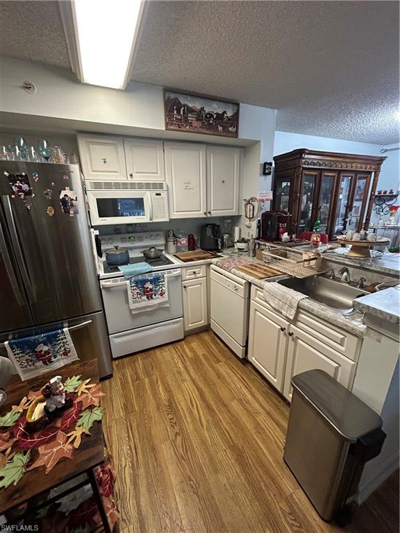Kitchen featuring fridge, white range, light wood-style floors, white cabinetry, and a textured ceiling