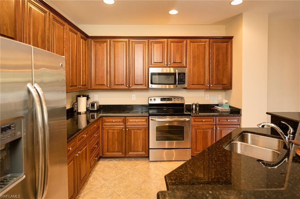 Kitchen with stainless steel appliances, dark stone counters, brown cabinetry, recessed lighting, and light tile patterned flooring
