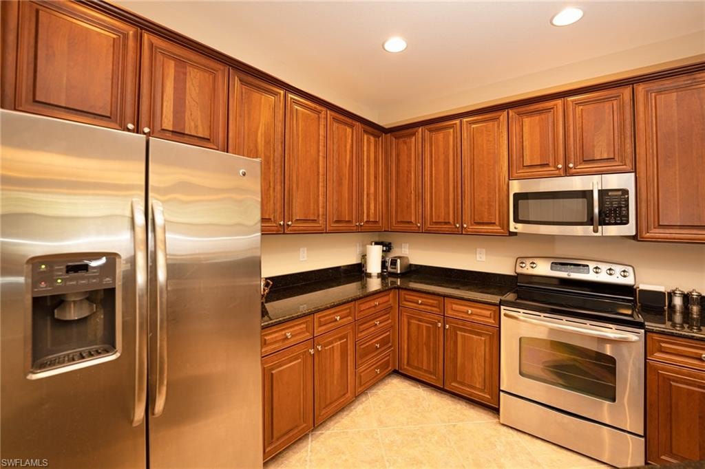 Kitchen featuring stainless steel appliances, brown cabinetry, dark stone countertops, and recessed lighting