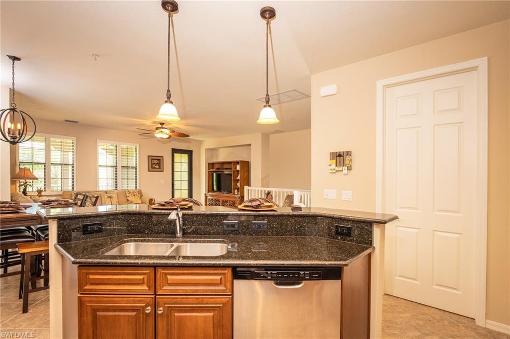 Kitchen with stainless steel dishwasher, light tile patterned floors, pendant lighting, dark stone counters, and open floor plan