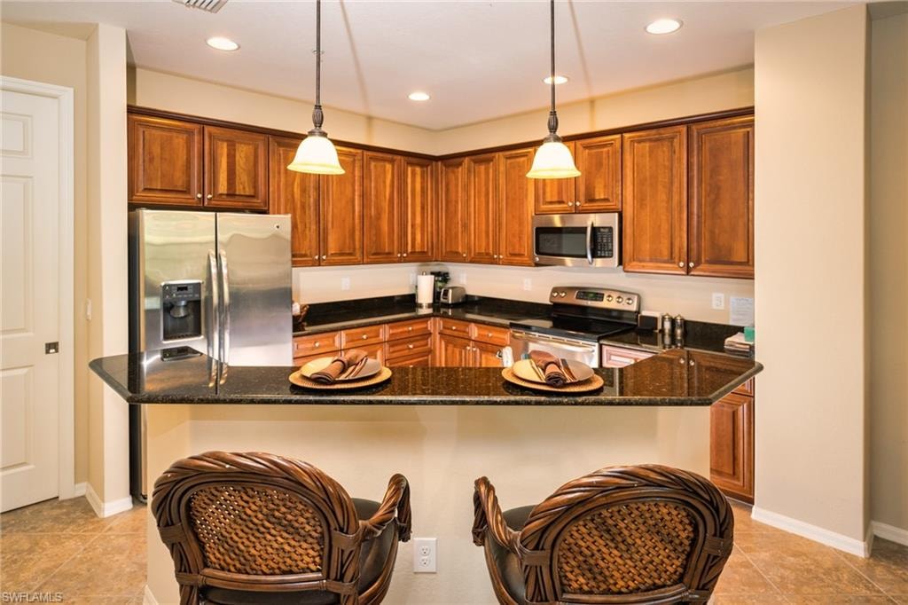 Kitchen with stainless steel appliances, dark stone counters, brown cabinetry, and recessed lighting