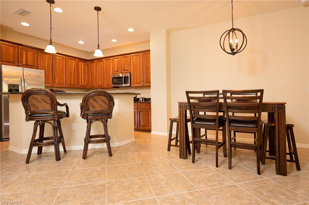 Kitchen with hanging light fixtures, stainless steel appliances, a kitchen breakfast bar, brown cabinets, and recessed lighting