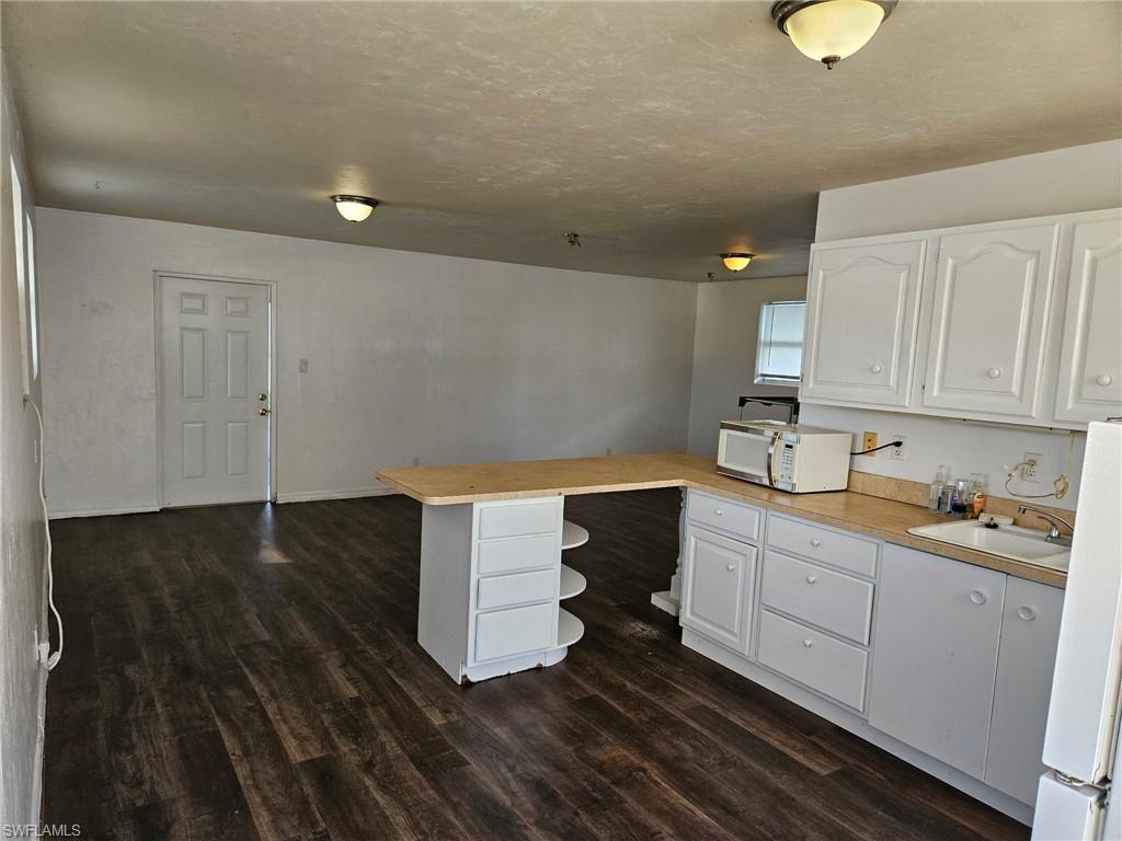 Kitchen with a peninsula, light countertops, white cabinets, white appliances, and a textured ceiling