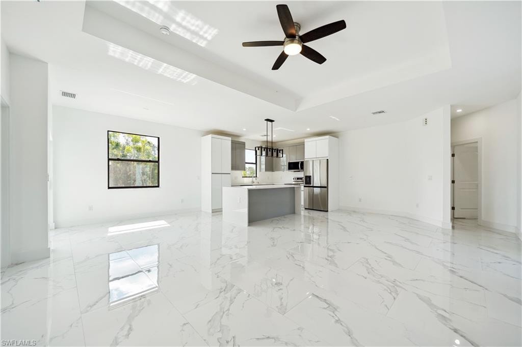 Kitchen featuring open floor plan, stainless steel appliances, a tray ceiling, light marble finish flooring, and light countertops