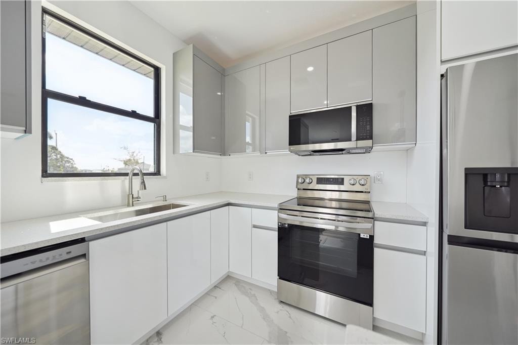 Kitchen with stainless steel appliances, modern cabinets, light marble finish flooring, and light stone countertops