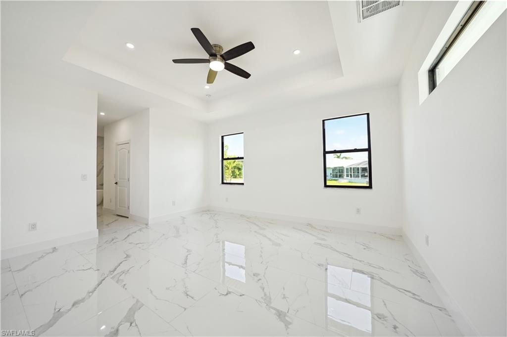 Unfurnished room with recessed lighting, a tray ceiling, light marble finish flooring, and a ceiling fan