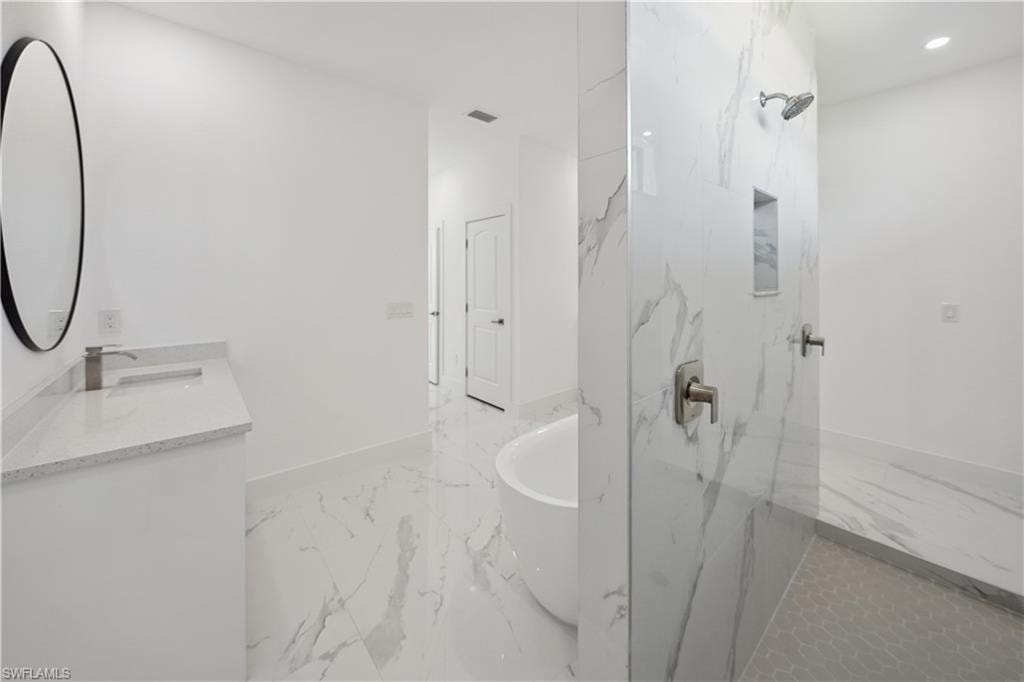 Full bathroom with a freestanding tub, a marble finish shower, light marble finish floors, vanity, and recessed lighting