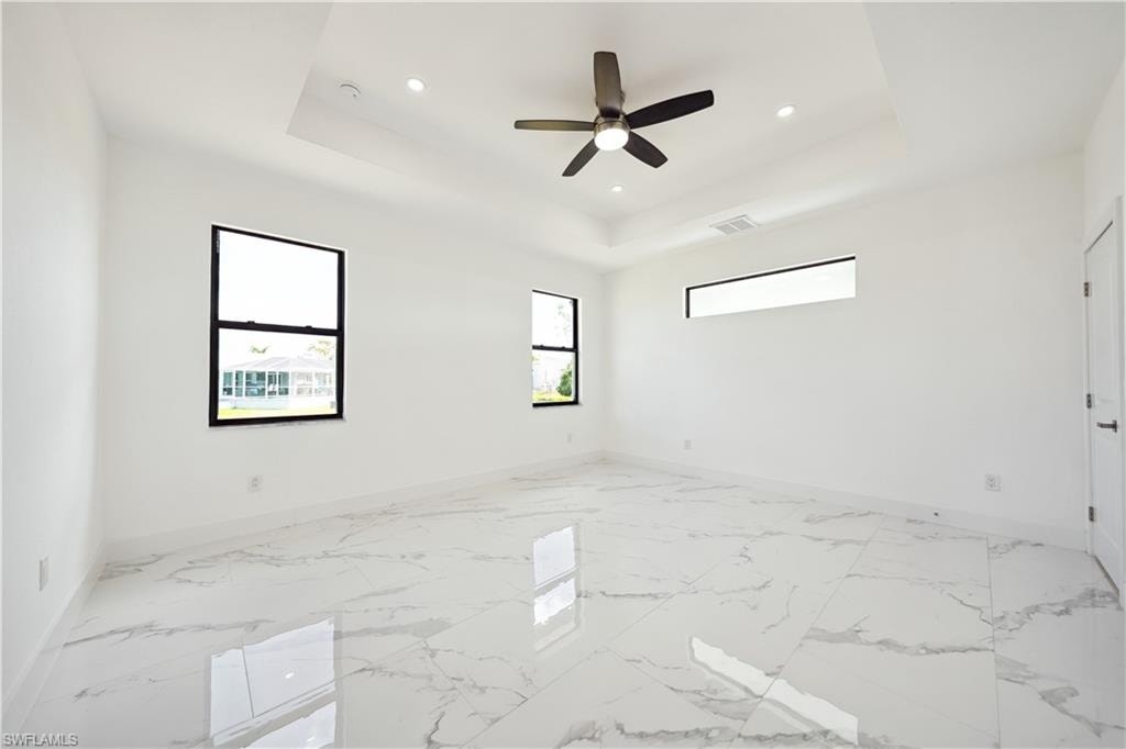 Spare room featuring light marble finish floors, recessed lighting, a tray ceiling, and a ceiling fan