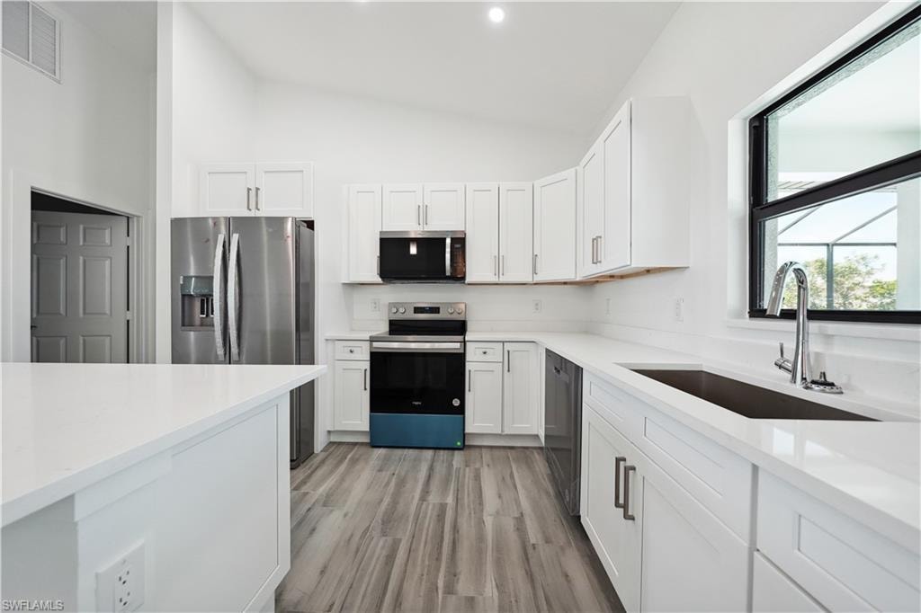 Kitchen with appliances with stainless steel finishes, white cabinetry, light stone countertops, and high vaulted ceiling