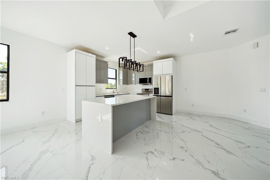 Kitchen featuring appliances with stainless steel finishes, a center island, white cabinets, light marble finish floors, and recessed lighting