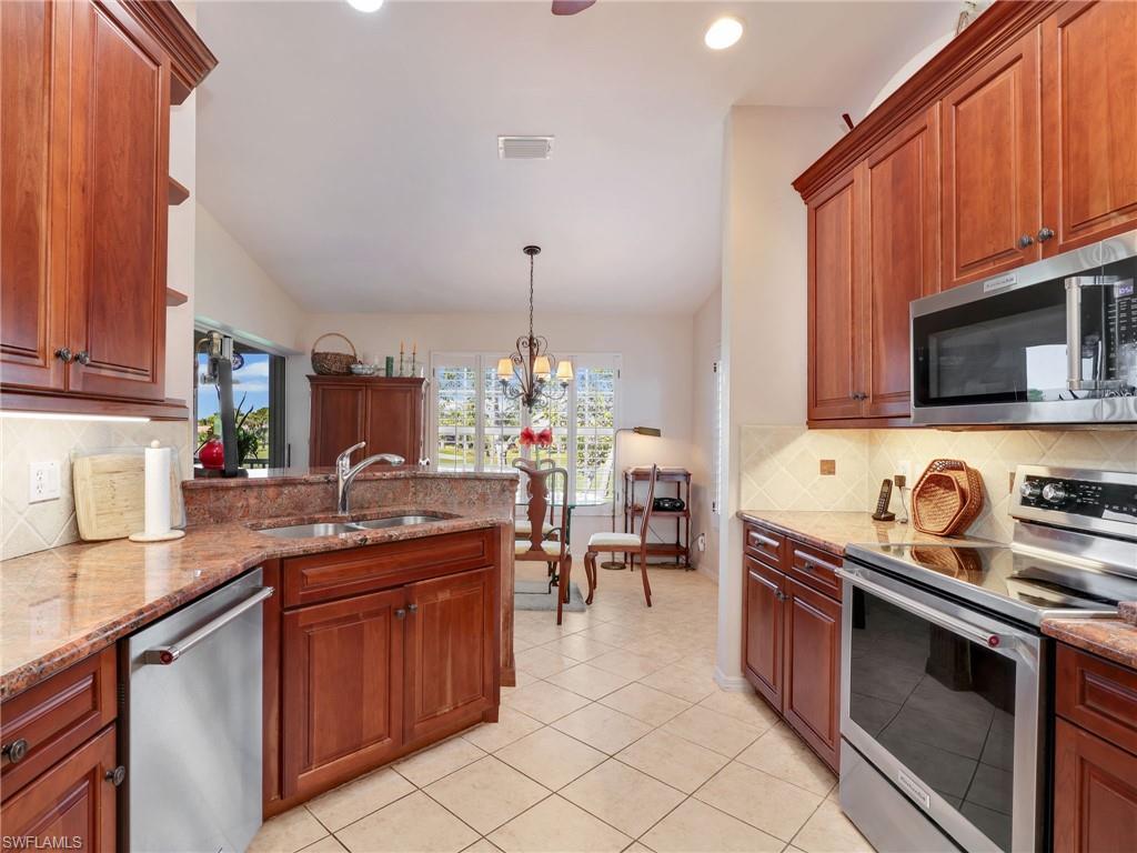 Kitchen with 42" custom Walnut cabinetry, backsplash, stainless steel appliances, granite countertops, decorative light fixtures, and a peninsula