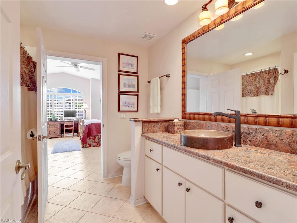 Ensuite bathroom with a shower with shower curtain, vanity, light tile patterned flooring, ceiling fan, and vaulted ceiling