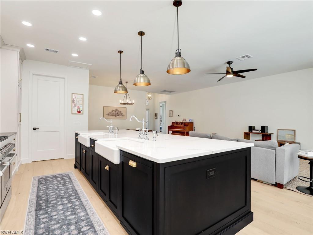 Kitchen featuring dark cabinets, a kitchen island with sink, open floor plan, hanging light fixtures, and light stone countertops