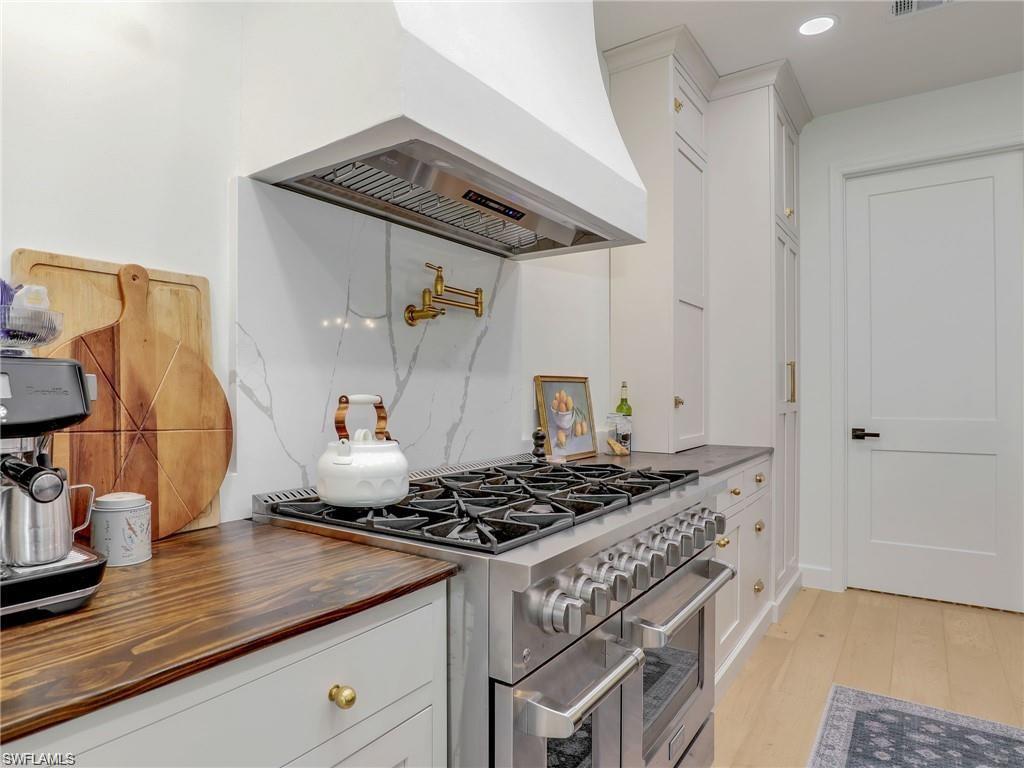 Kitchen with double oven range, white cabinets, premium range hood, light wood-style floors, and wood counters