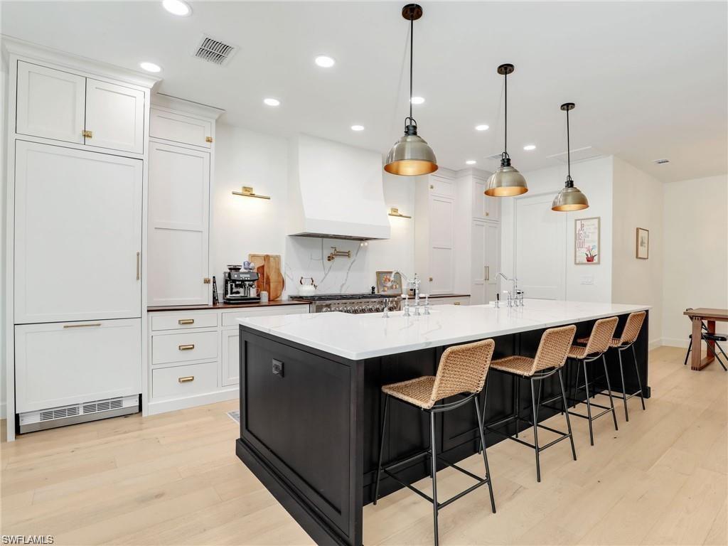 Kitchen featuring a large island with sink, white cabinetry, hanging light fixtures, custom exhaust hood, and a breakfast bar area