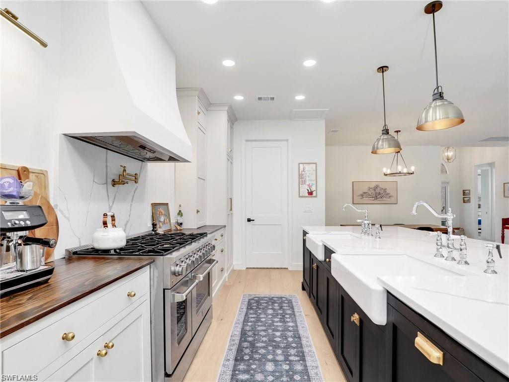 Kitchen with dark cabinetry, range with two ovens, decorative light fixtures, premium range hood, and white cabinets