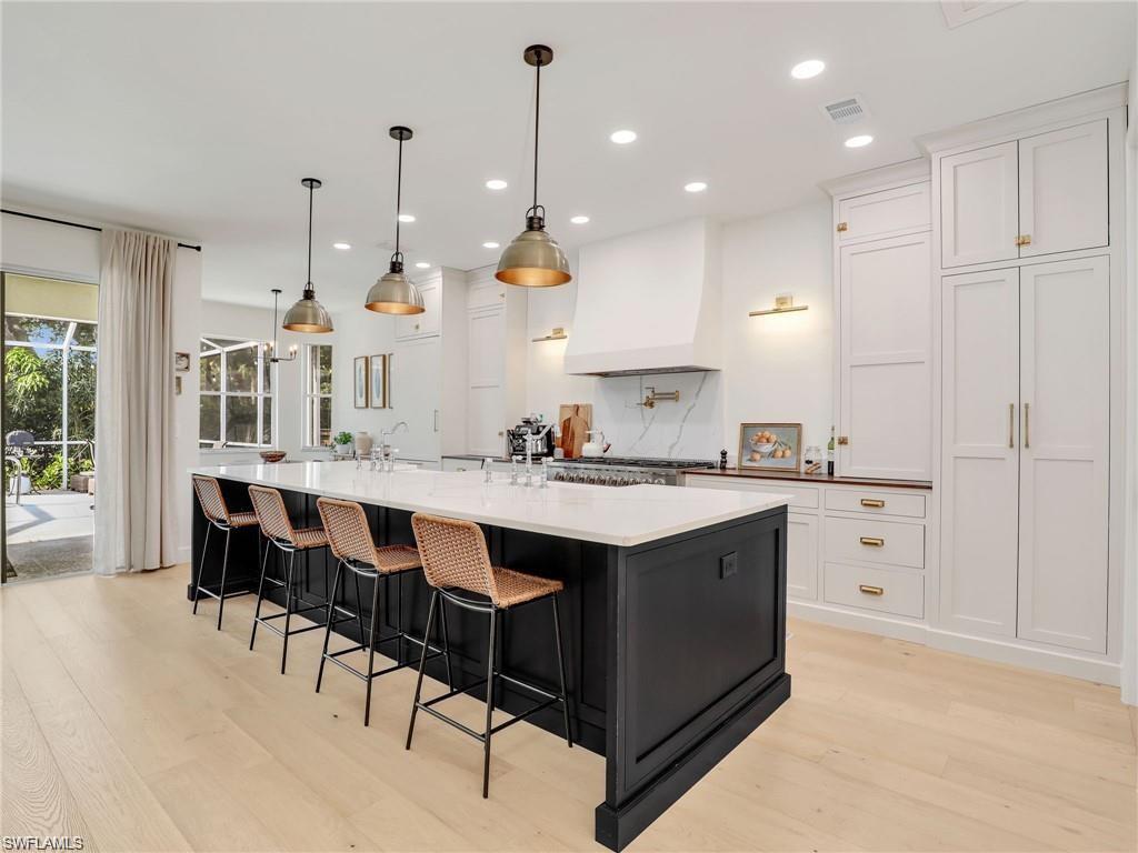Kitchen featuring dark cabinetry, a spacious island, white cabinetry, custom exhaust hood, and recessed lighting