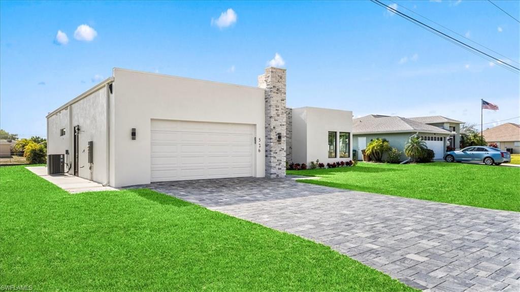 Modern home featuring a front lawn, stucco siding, decorative driveway, a garage, and a chimney