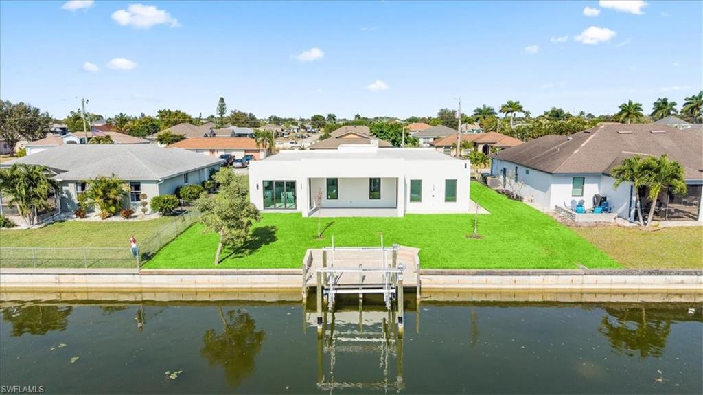 Back of property featuring a water view, a patio area, a yard, boat lift, and a residential view