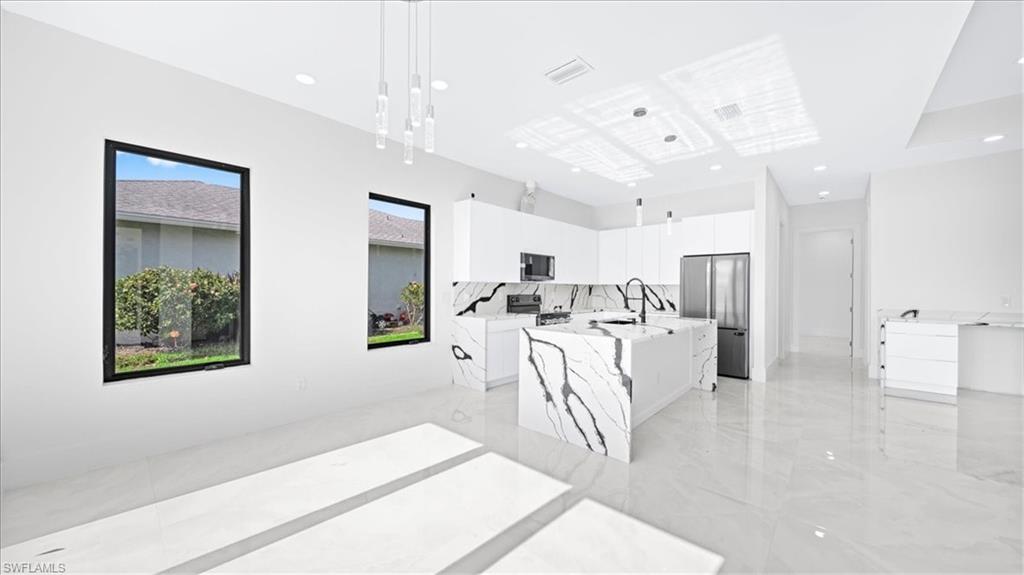 Kitchen with appliances with stainless steel finishes, white cabinetry, a center island with sink, pendant lighting, and light marble finish floors