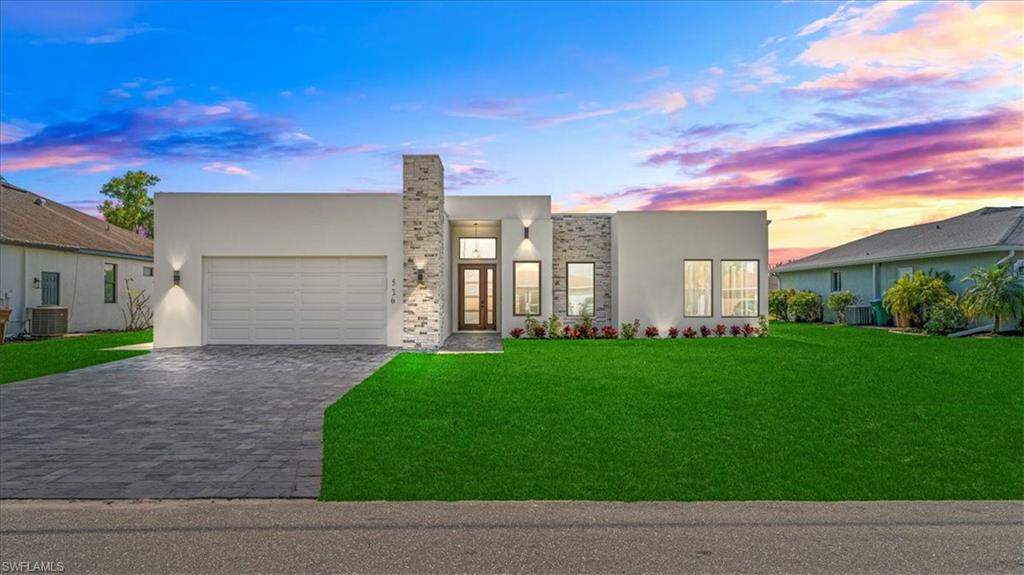 Contemporary house with decorative driveway, a front lawn, stucco siding, and a garage