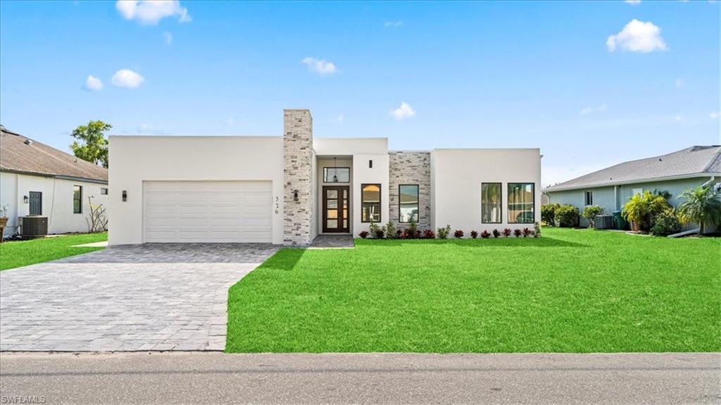 Contemporary house with decorative driveway, a front lawn, stucco siding, and an attached garage