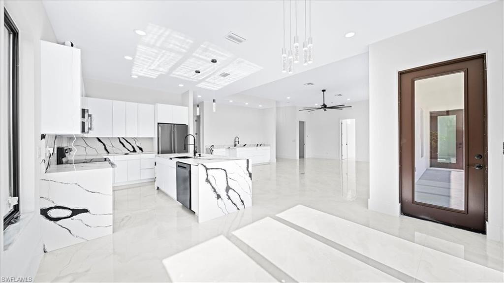 Kitchen featuring white cabinets, light stone countertops, a kitchen island with sink, freestanding refrigerator, and hanging light fixtures
