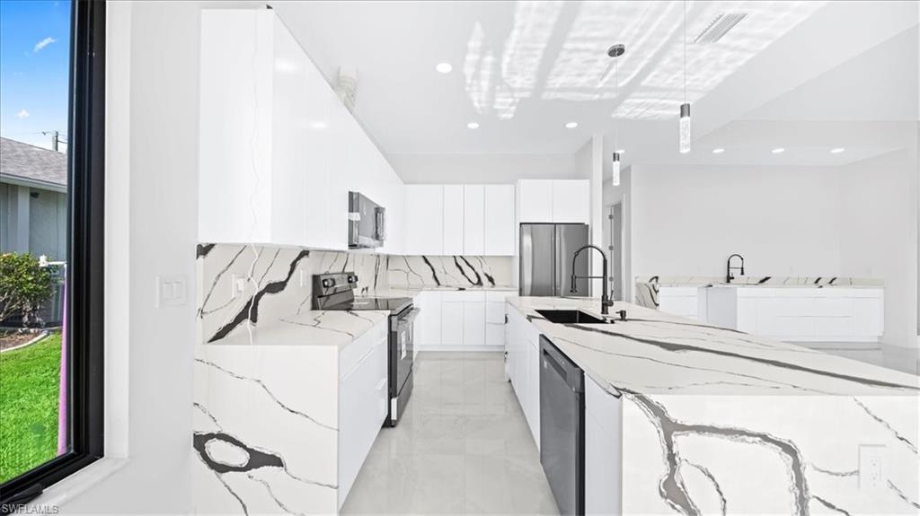 Kitchen with light stone counters, modern cabinets, stainless steel appliances, white cabinetry, and a center island with sink