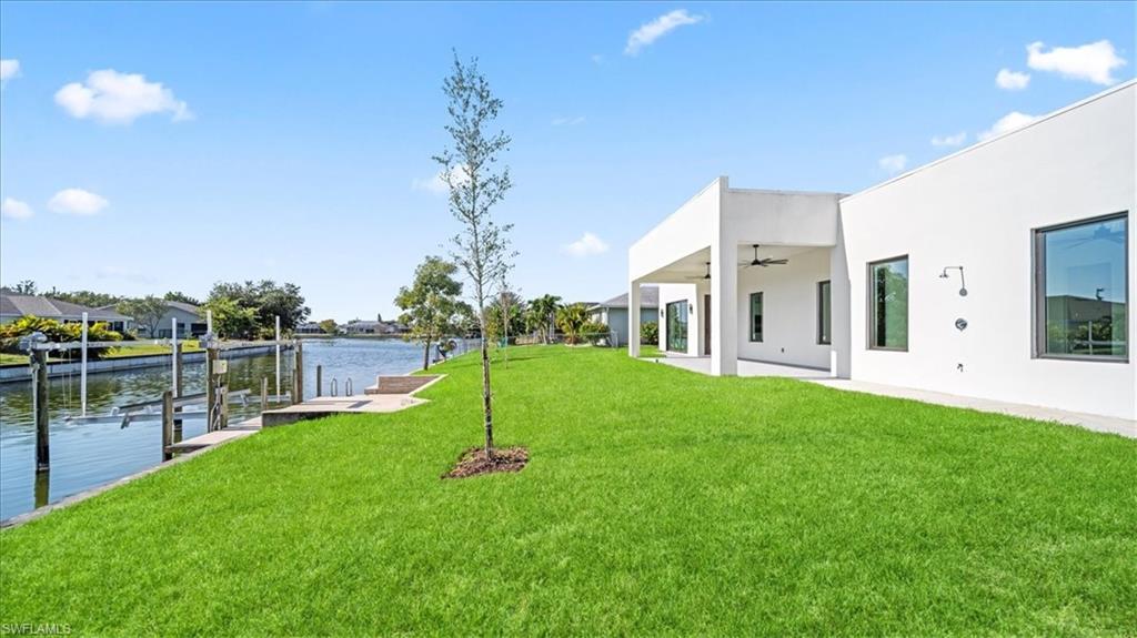 View of green lawn with a water view, a patio area, a dock, a ceiling fan, and boat lift