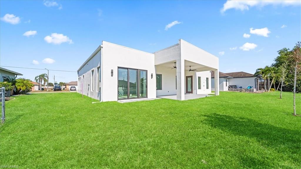 Back of property with a lawn, ceiling fan, a patio area, and stucco siding