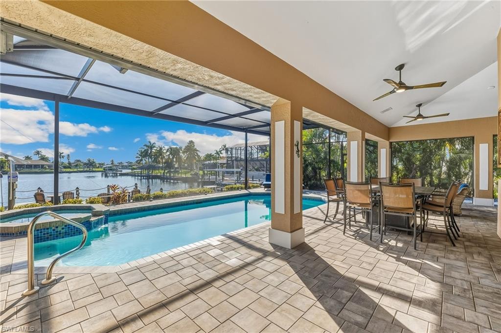 View of pool featuring a lanai, a patio area, a water view, outdoor dining space, and a pool with connected hot tub