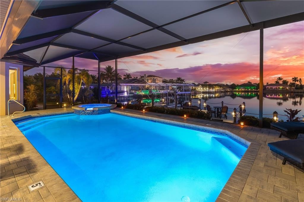 View of swimming pool featuring glass enclosure, a pool with connected hot tub, a patio area, a water view, and boat lift
