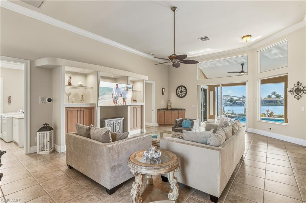 Living room with ornamental molding, a water view, washer and dryer, light tile patterned floors, and ceiling fan