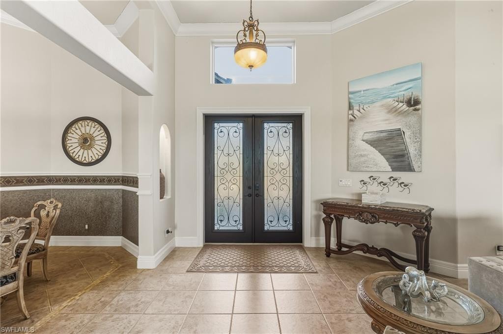 Foyer with french doors, ornamental molding, light tile patterned floors, a high ceiling, and arched walkways