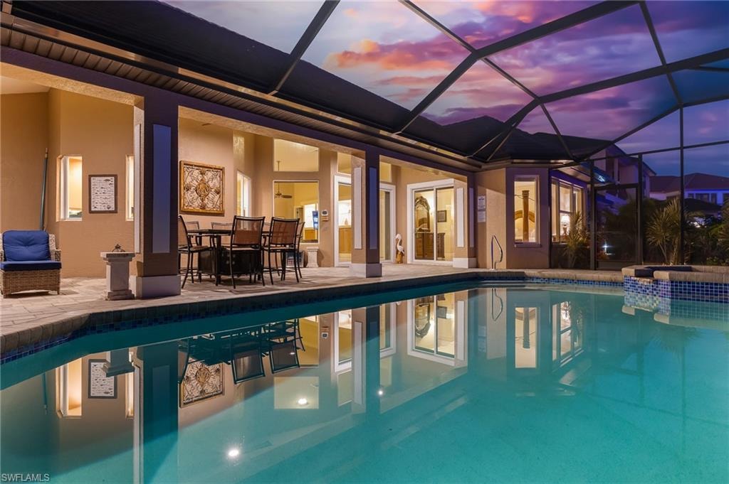 Pool at dusk featuring a patio area, glass enclosure, a pool with connected hot tub, a sunroom, and outdoor dining area