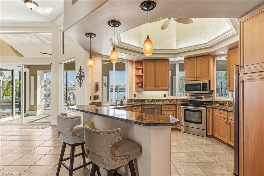 Kitchen with open shelves, appliances with stainless steel finishes, pendant lighting, dark stone counters, and ornamental molding