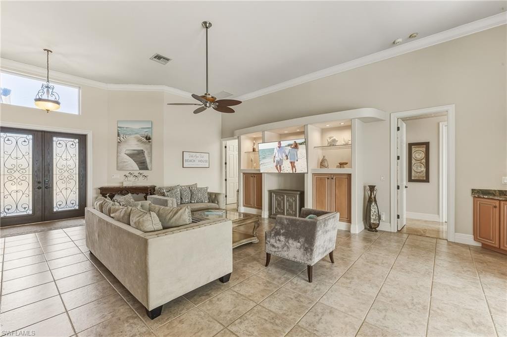 Living room with french doors, light tile patterned flooring, ornamental molding, and a ceiling fan
