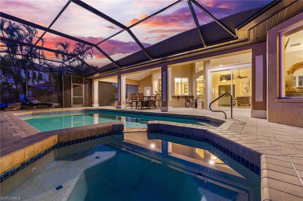 Pool at dusk with a patio area, a sunroom, a lanai, and a pool with connected hot tub