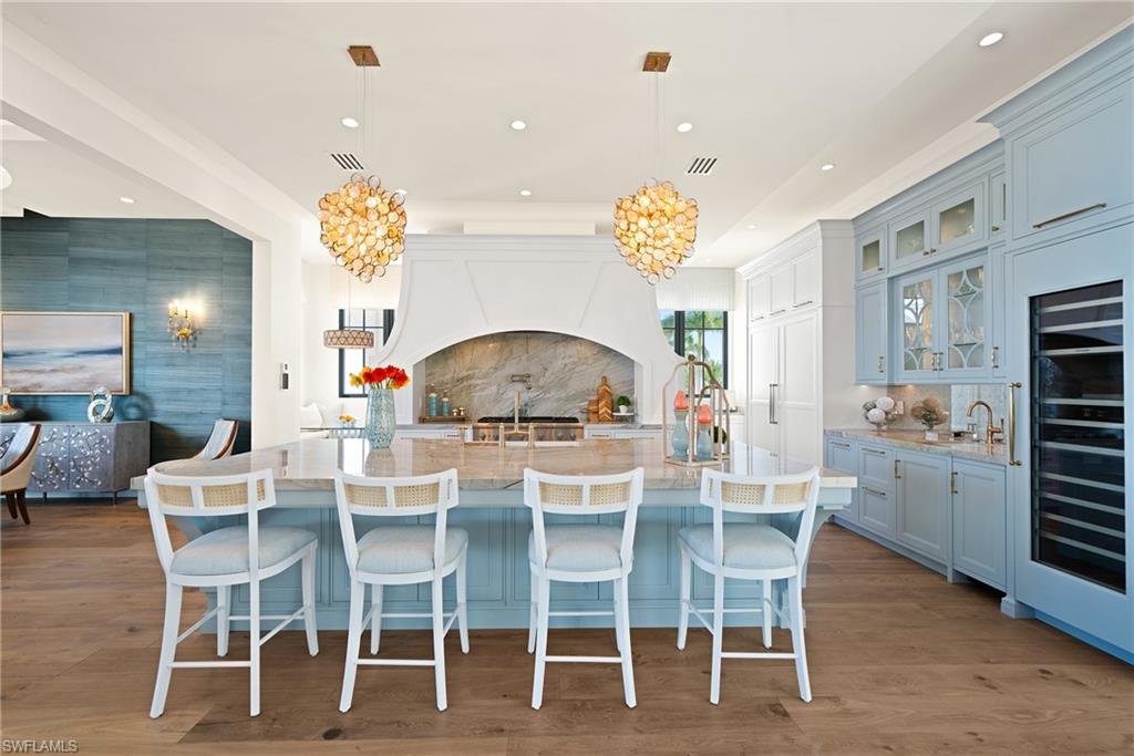 Kitchen with hanging light fixtures, light stone countertops, a large island, tasteful backsplash, and wine cooler