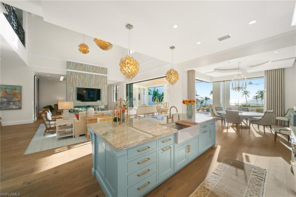 Kitchen with light stone counters, hanging light fixtures, dark wood-style floors, open floor plan, and an island with sink