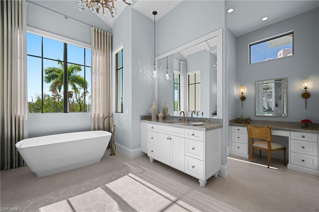 Bathroom featuring a chandelier, vanity, a soaking tub, and healthy amount of natural light