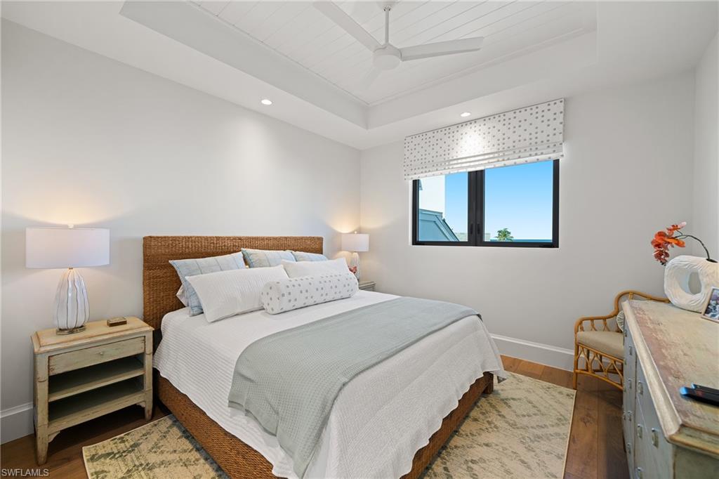 Bedroom with a raised ceiling, wood finished floors, and ceiling fan