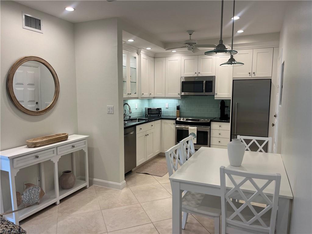 Kitchen with appliances with stainless steel finishes, glass insert cabinets, white cabinets, hanging light fixtures, and recessed lighting