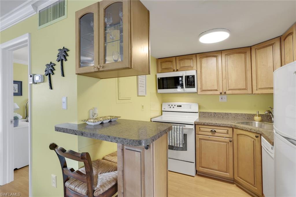 Kitchen featuring sink, crown molding, white appliances, a breakfast bar area, and light wood-type flooring