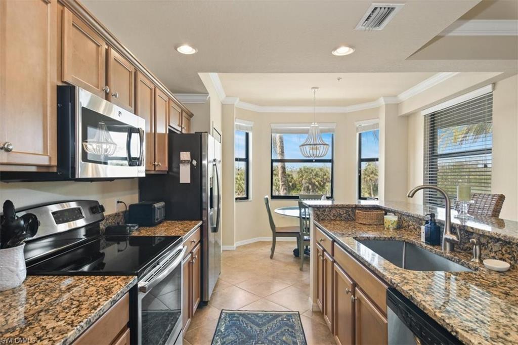 Kitchen featuring stainless steel appliances, dark stone countertops, crown molding, wood finish cabinetry, and decorative light fixtures