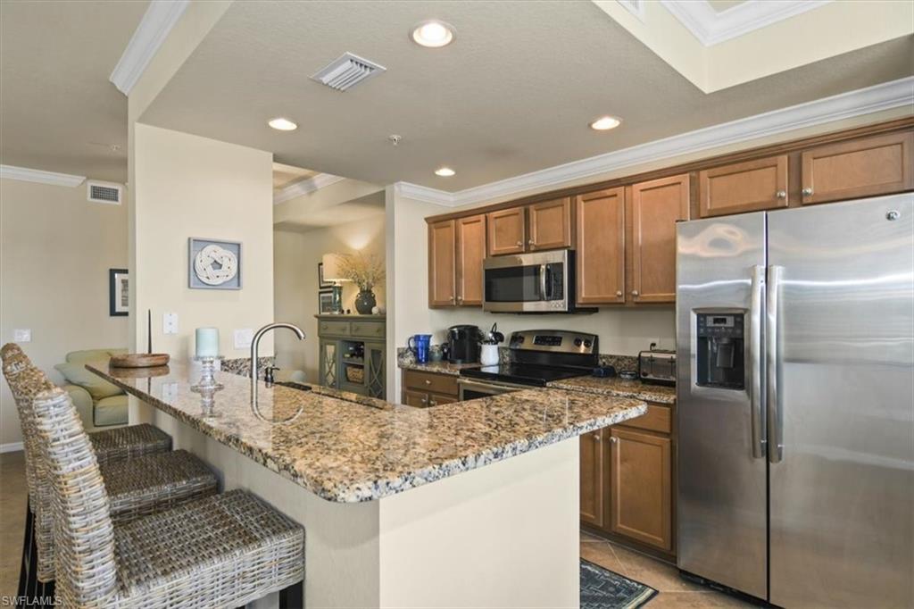 Kitchen featuring stainless steel appliances, a peninsula, ornamental molding, wood finish cabinetry, and dark stone counters