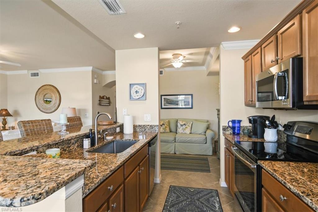 Kitchen featuring ceiling fan, stainless steel appliances, wood finish cabinets, dark stone countertops, and ornamental molding