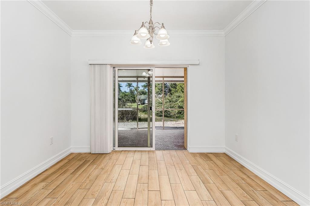 Dining room featuring wood-style tiled floors, a chandelier, and crown molding, leading to screened lanai in backyard