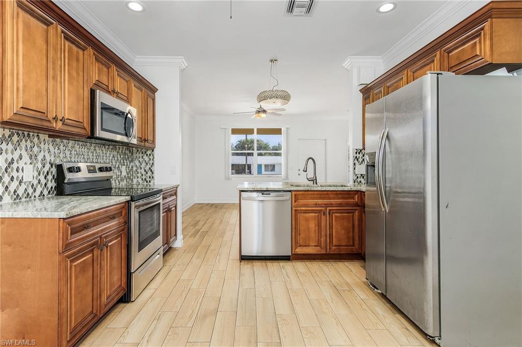 Kitchen featuring appliances with stainless steel finishes, a peninsula, light stone counters, brown cabinets, and crown molding